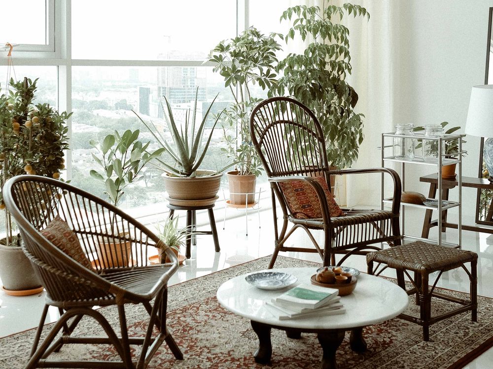 Bright apartment living area with rattan chairs, a round marble table and indoor plants by the windows