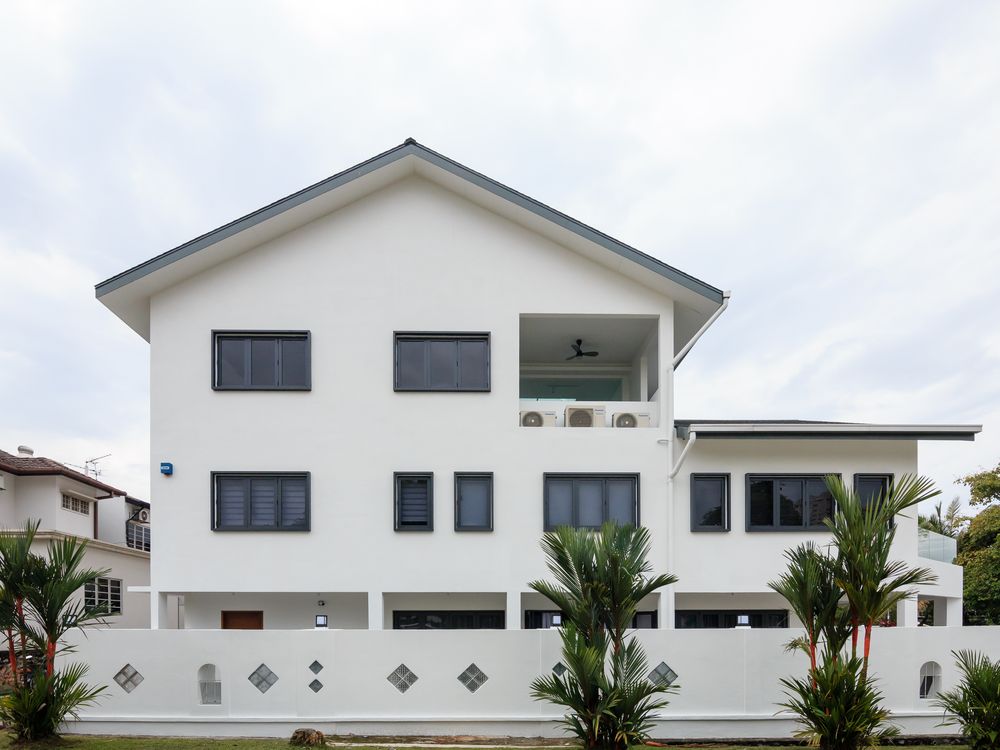 White three-storey corner house with dark window frames and a low boundary wall