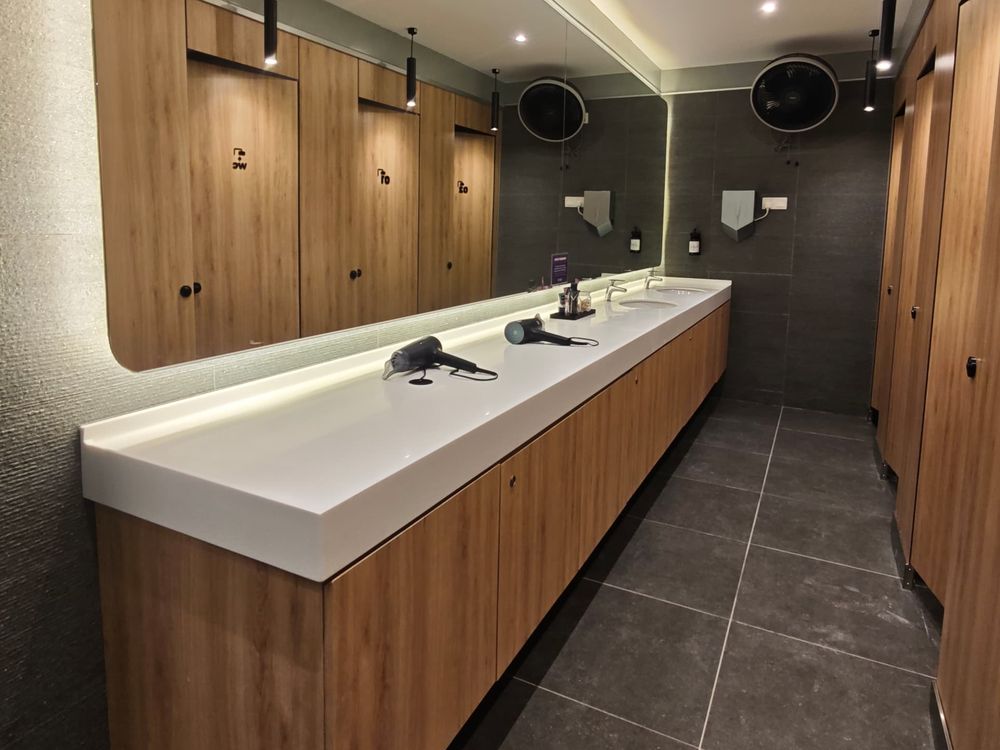 Changing room with a long vanity counter, backlit mirror and timber-finish cubicles
